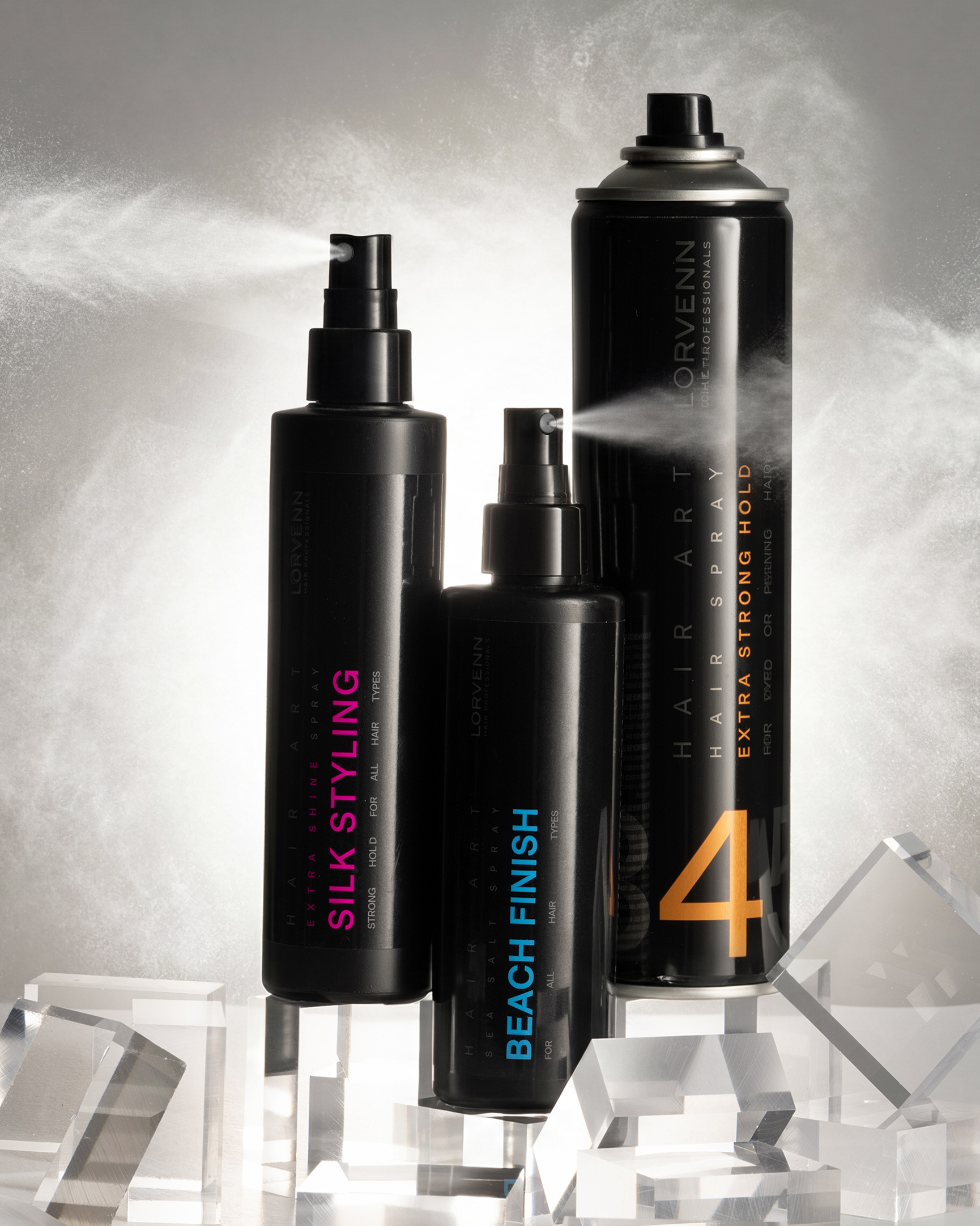 Lorvenn hair spray bottles spraying mist next to clear acrylic blocks against a gray background.